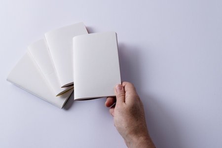 Hand of caucasian woman notebook over other notebooks with copy space on white background. Literature, reading, leisure time and books.の写真素材