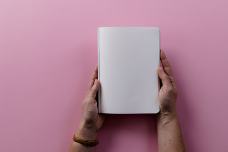 Hands of caucasian woman holding book with copy space on pink background. Literature, reading,...