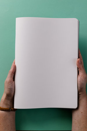 Close up of hands of caucasian woman holding book with copy space on green background. Literature, reading, leisure time and books.の写真素材