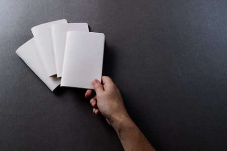 Hand of caucasian woman holding a notebook over other notebooks with copy space on grey background....