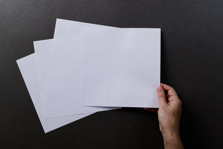 Hand of caucasian woman holding piece of paper over paper pieces with copy space on black...