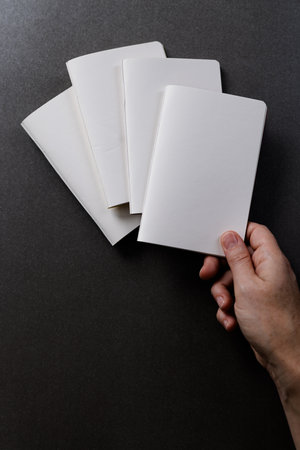 Hand of caucasian woman holding a notebook over other notebooks with copy space on black background....