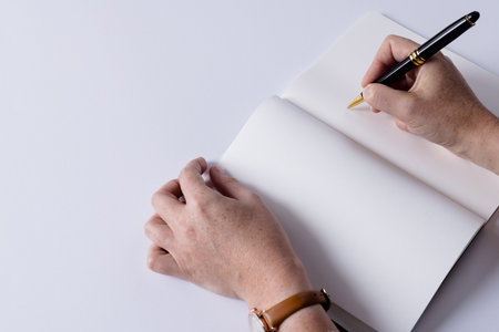 Hands of caucasian woman holding pen and writing in notebook with copy space on white background. Literature, writing, leisure time and books.の写真素材