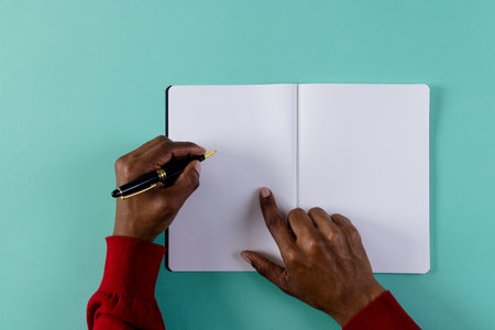 Hands of biracial man holding pen, writing in notebook with copy space on green background....