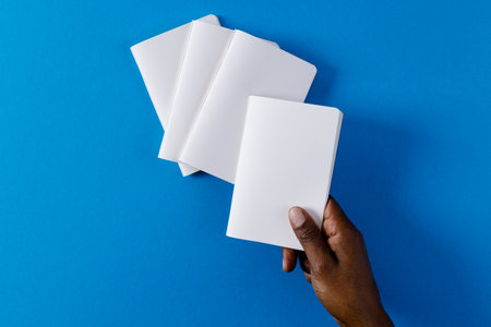 Hand of biracial man holding notebook over notebooks with copy space on blue background. Literature,...