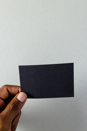 Vertical image of hand of biracial man with black business card with copy space on white background....