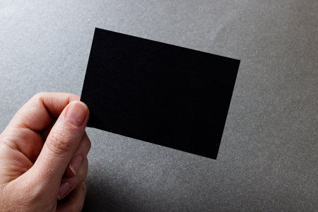 Hand of caucasian woman holding black business card with copy space on grey background. Business, business card, stationery and writing space concept.の写真素材