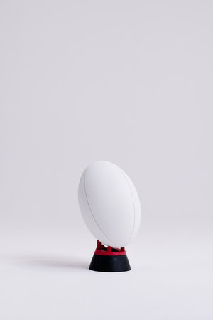 White rugby ball on red and black stand with copy space on white background. Rugby, sport, international, competition and games digitally generated image.の写真素材