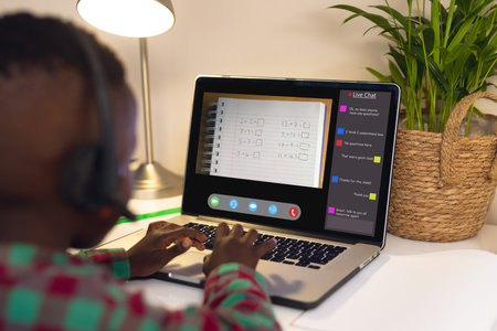 African american boy wearing headphones and learning mathematics over video call on laptop....