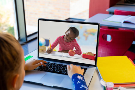 Rear view of a caucasian girl having a video call with african american girl on laptop at school. Distant learning online education conceptの写真素材