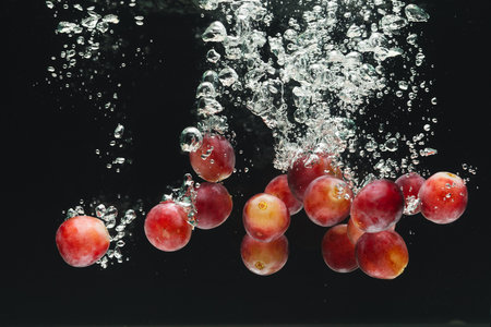 Close up of red grapes falling into water with copy space on black background. Fruit, vegan food and colour concept.の写真素材