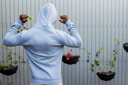 Rear view of african american man wearing grey hooded sweatshirt against white fence, copy space....