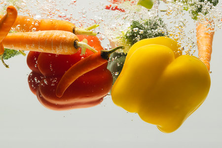 Close up of fresh vegetables falling into water with copy space on white background. Vegetables,...