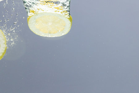 Close up of lemon slices falling into water with copy space on grey background. Fruit, vegan food and colour concept.の写真素材