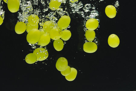 Close up of white grapes falling into water with copy space on black background. Fruit, vegan food...