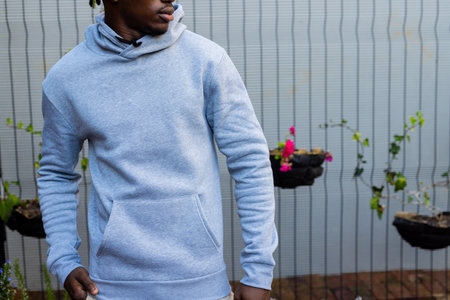 Midsection of african american man wearing grey hooded sweatshirt against white fence, copy space....
