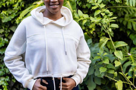 Midsection of happy african american woman wearing white hooded sweatshirt standing in garden. Fashion, casual clothing and leisurewear, unaltered.の写真素材