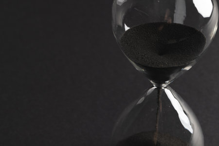 Close up of hourglass with black sand and copy space on black background. Time, timekeeping, shape and colour concept.の写真素材