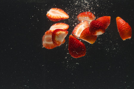 Close up of strawberries falling into water with copy space on black background. Fruit, vegan food and colour concept.の写真素材