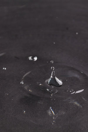 Close up of water drop falling into water with ripples and copy space on black background. Water, liquid and colour concept.の写真素材