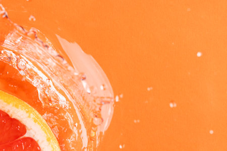 Close up of red grapefruit slice in water with copy space on orange background. Fruit, vegan food and colour concept.の写真素材