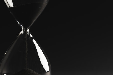 Close up of hourglass with black sand and copy space on black background. Time, timekeeping, shape...