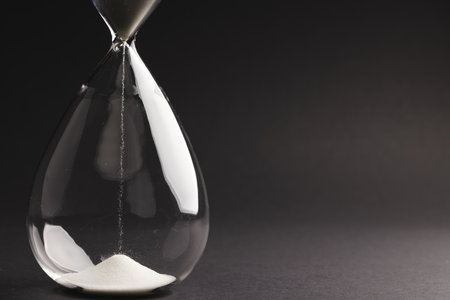 Close up of hourglass with white sand and copy space on black background. Time, timekeeping, shape...