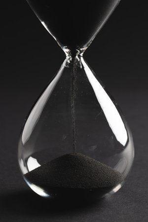 Close up of hourglass with black sand and copy space on black background. Time, timekeeping, shape...
