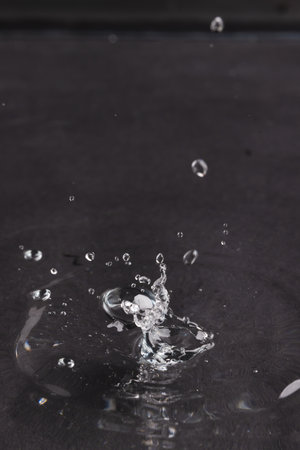 Close up of water drop falling into water with ripples and copy space on black background. Water, liquid and colour concept.の写真素材