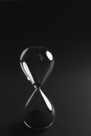 Close up of hourglass with black sand and copy space on black background. Time, timekeeping, shape...