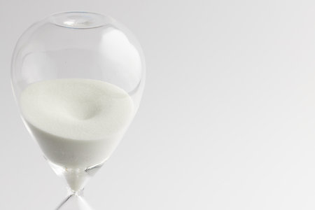 Close up of hourglass with white sand and copy space on white background. Time, timekeeping, shape...