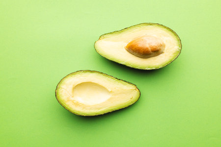 Close up of two halves of avocado and copy space on green background. Vegetable, food, freshness and...