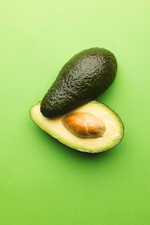 Close up of two halves of avocado and copy space on green background. Vegetable, food, freshness and...