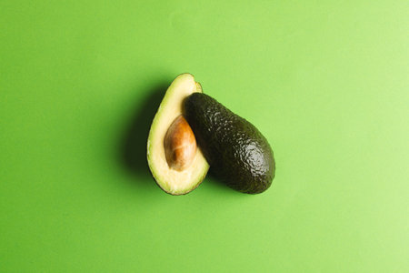 Close up of two halves of avocado and copy space on green background. Vegetable, food, freshness and...