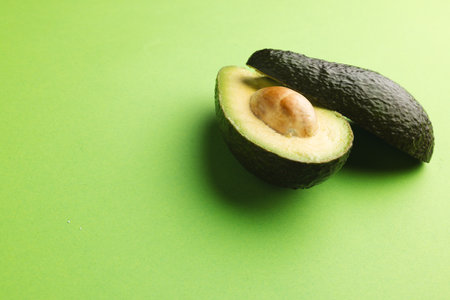 Close up of two halves of avocado and copy space on green background. Vegetable, food, freshness and...