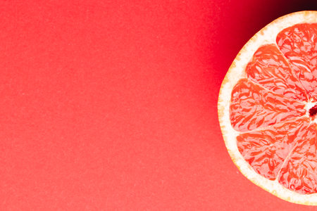 Close up of half of red grapefruit and copy space on red background. Fruit, food, freshness and...