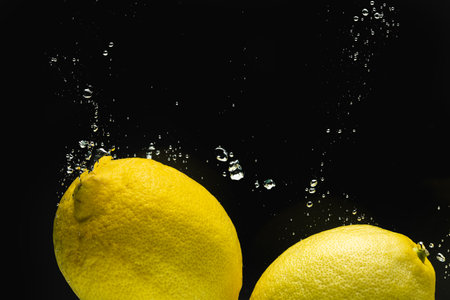 Close up of lemons falling into water with copy space on black background. Fruit, food, freshness and colour concept.の写真素材