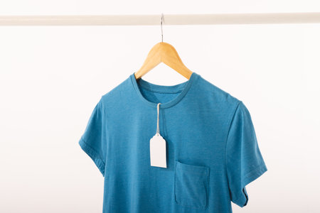 Blue t shirt with tag on hanger hanging from clothes rail with copy space on white background. Fashion, clothes, colour and fabric concept.の写真素材