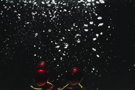 Close up of cherries falling into water with copy space on black background. Fruit, food, freshness and colour concept.の写真素材