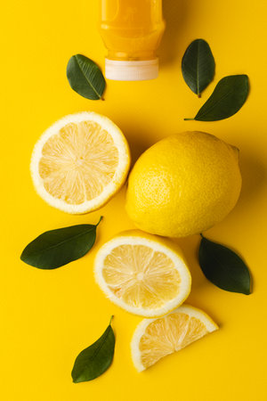Close up of bottle with juice, lemon, lemon slices and leaves with copy space on yellow background. Fruit, food, freshness and colour concept.の写真素材