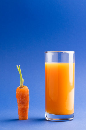Close up of carrot and glass of carrot juice with copy space on blue background. Vegetable, drink, food, freshness and colour concept.の写真素材