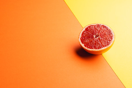Close up of half of red grapefruit and copy space on orange and yellow background. Fruit, food, freshness and colour concept.の写真素材