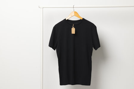 Black t shirt with tag hanging from clothes rack with copy space on white background. Fashion, clothes, colour and fabric concept.の写真素材