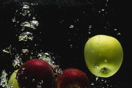 Close up of apples falling into water with copy space on black background. Fruit, food, freshness and colour concept.の写真素材