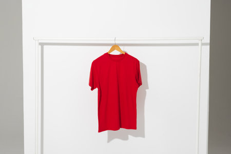 Red t shirt on hanger hanging from clothes rail with copy space on white background. Fashion,...