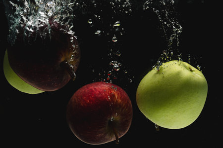 Close up of apples falling into water with copy space on black background. Fruit, food, freshness and colour concept.の写真素材