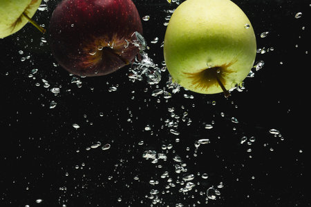 Close up of apples falling into water with copy space on black background. Fruit, food, freshness and colour concept.の写真素材
