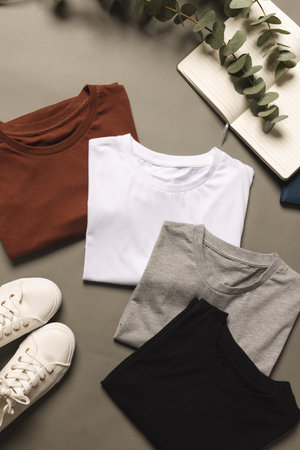 Multi coloured t shirts, shoes and notebook with copy space on grey floor background. Fashion,...