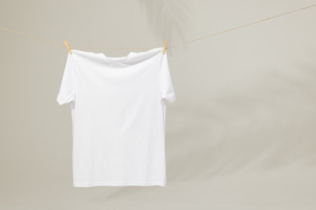 White t shirt hanging from clothes line with pegs and copy space on grey background. Fashion, clothes, colour and fabric concept.の写真素材