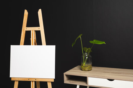 White canvas on wooden easel and copy space with desk and plant on black background. Signage, writing space and advertising concept.の写真素材